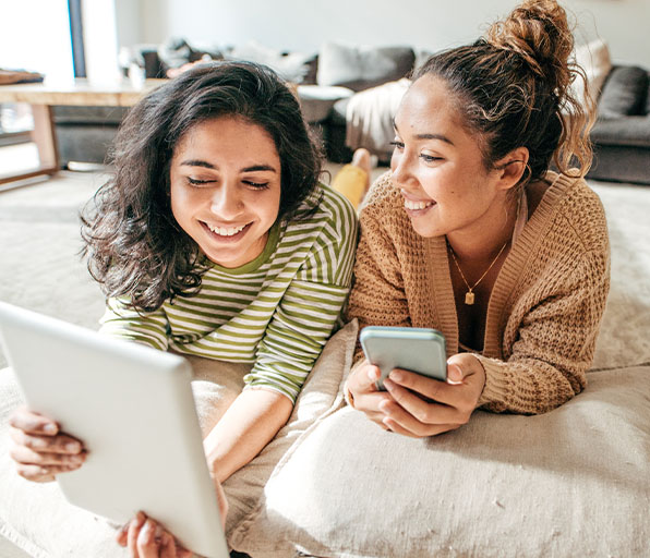 Two young women laying on floor looking at tablet